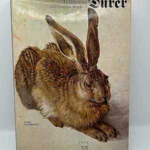 May include: A book cover displaying "The Drawings and Graphic Works of Dürer" with a detailed illustration of a brown rabbit. The cover includes the text "Fedja Anzelewsky" and the year "1502". The book has a vintage appearance.