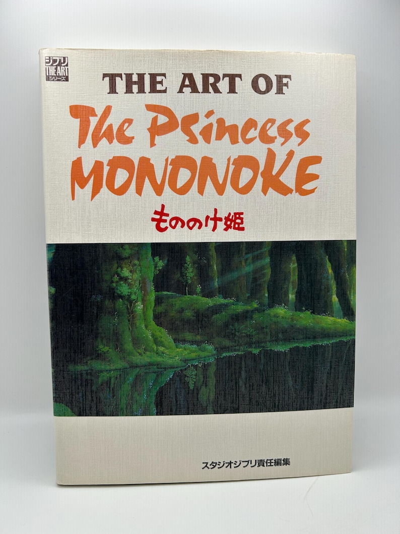 May include: A hardcover book titled The Art of The Princess Mononoke with a cream-colored cover featuring the title in brown and orange text, Japanese characters, and a dark green forest illustration reflected in a body of water at the bottom.