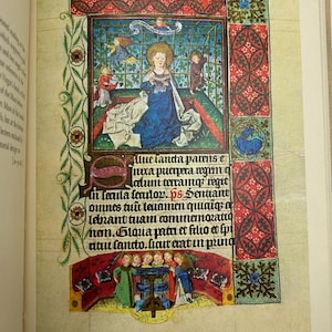 May include: A detailed illuminated manuscript page featuring a central illustration of a woman in a blue gown with a gold halo. The page is adorned with intricate borders in red, green, and gold, and includes Latin text.