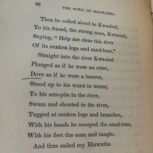 May include: Open book page with text from "The Song of Hiawatha." The page number 96 is visible at the top left. The text describes a scene with characters Kwasind and Hiawatha, and mentions a river and sunken logs.
