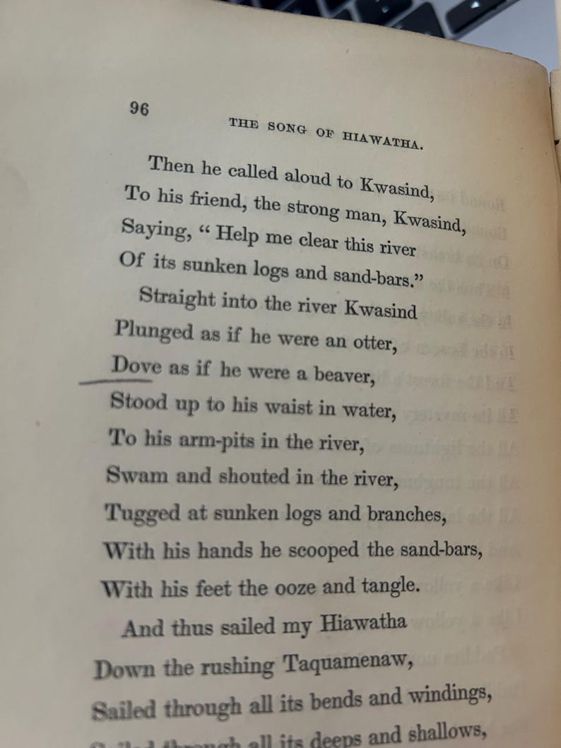 May include: Open book page with text from "The Song of Hiawatha." The page number 96 is visible at the top left. The text describes a scene with characters Kwasind and Hiawatha, and mentions a river and sunken logs.