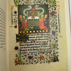 May include: A page from an illuminated manuscript featuring a central illustration of figures in red and gold robes, with text in Latin. The page is decorated with floral and foliate borders in green, red, and blue, set against a cream-colored background.