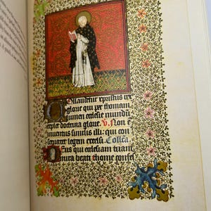 May include: Open book with a detailed illustration of a religious figure in a black and white robe, holding a book. The illustration is set against a red background, surrounded by floral patterns and text.
