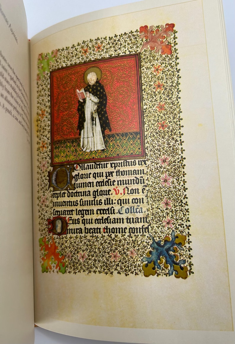 May include: Open book with a detailed illustration of a religious figure in a black and white robe, holding a book. The illustration is set against a red background, surrounded by floral patterns and text.