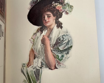 May include: An illustration of a woman wearing a large black hat adorned with flowers. She is dressed in a light-colored gown with green and blue accents. The artwork is a vintage print, likely from a book or magazine.