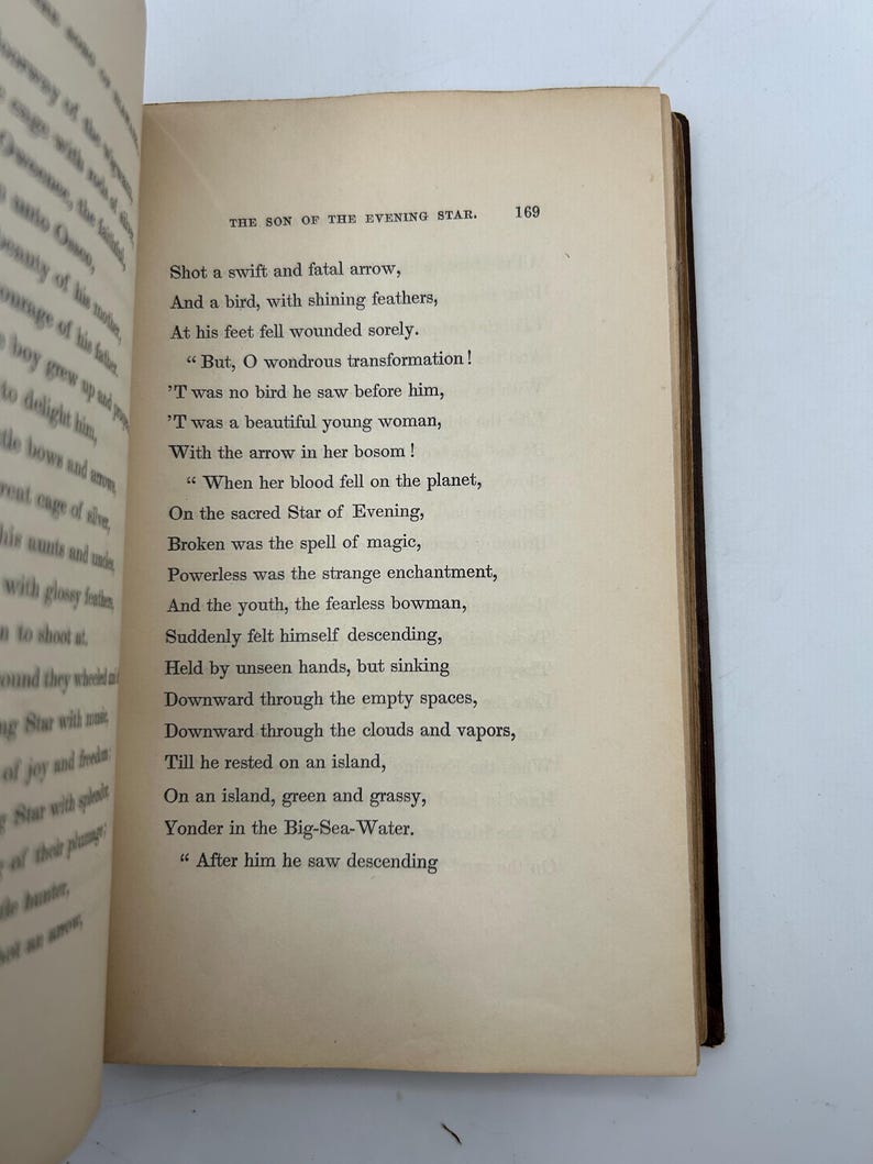 May include: Open book with aged, yellowed pages. The text on the right page is titled "THE SON OF THE EVENING STAR" and includes poetry. The book's spine is dark brown, and the edges of the pages are rough.