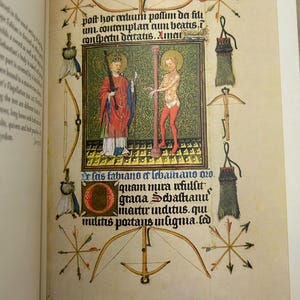 May include: An illuminated manuscript page featuring two figures within a green and gold frame. The page is adorned with bows, arrows, and text in Latin. The figures are dressed in red and white robes.