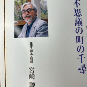 May include: A book with a portrait of a man wearing glasses and a gray blazer. Japanese text is printed on the right side of the book. The text on the left side of the book is in Japanese.