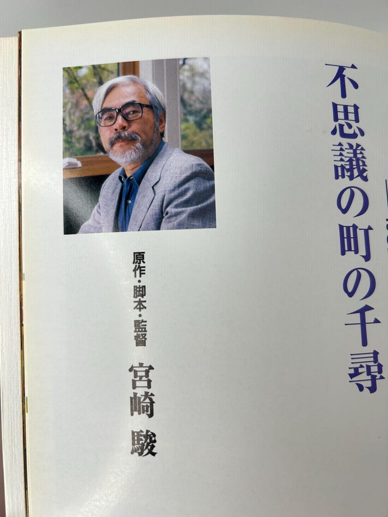 May include: A book with a portrait of a man wearing glasses and a gray blazer. Japanese text is printed on the right side of the book. The text on the left side of the book is in Japanese.