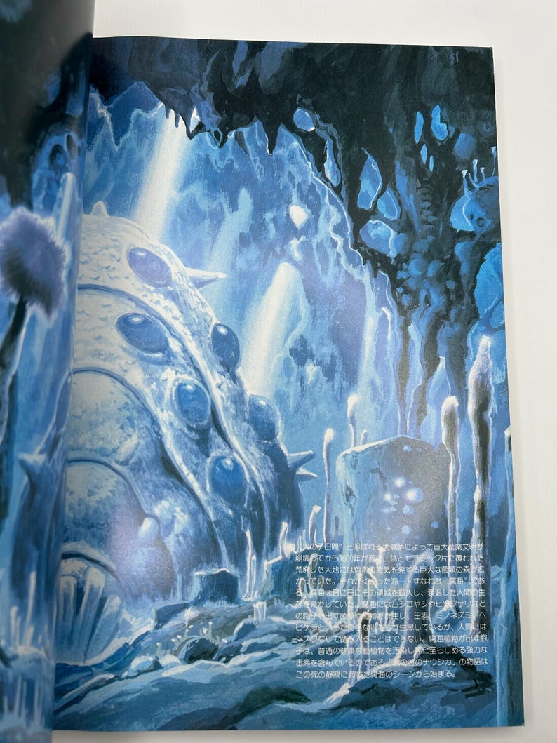 May include: An illustration of a blue and white fantasy landscape with cave-like structures and a large, textured, egg-shaped object. The scene is lit with a cool, ethereal glow, suggesting an underwater or otherworldly environment. The image has a detailed, artistic style.
