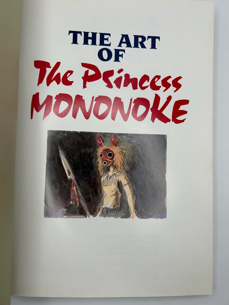 May include: A book cover titled THE ART OF The Princess MONONOKE in dark blue and red text. Below the title is a watercolor illustration of a figure wearing a red and white mask with pointed ears, holding a spear against a dark gray background.