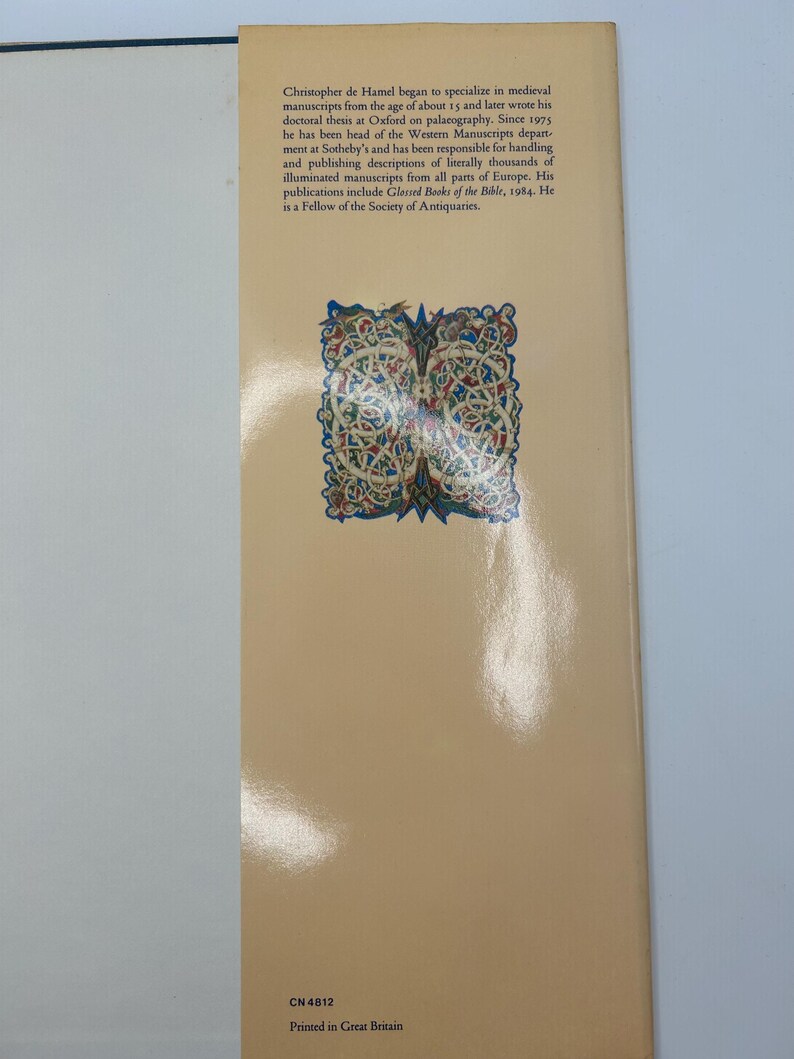Op de afbeelding: De achterkant van een boek met een gedetailleerde illustratie van een middeleeuws knoopontwerp in goud en rood. De tekst op de achterkant beschrijft de expertise van de auteur in middeleeuwse manuscripten en zijn werk bij Sotheby's.