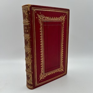 May include: A red leather-bound book with gold-leaf detailing and a decorative border around the cover. The book's title, "The Works of", is visible on the spine.