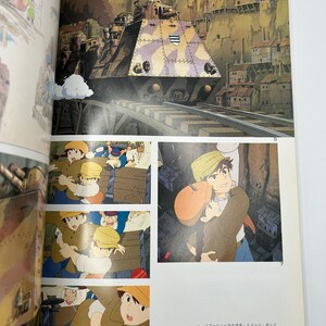May include: An illustration from a Japanese animated film featuring a large, camouflaged train on tracks, set against a backdrop of a town built into a cliffside. Below, several panels depict characters in action, with text in Japanese.