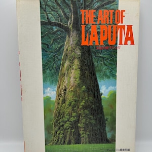 May include: A hardcover book titled "THE ART OF LAPUTA" with a vibrant illustration of a large tree. The cover art features a detailed painting of the tree's trunk and canopy, with green foliage and a blue sky.