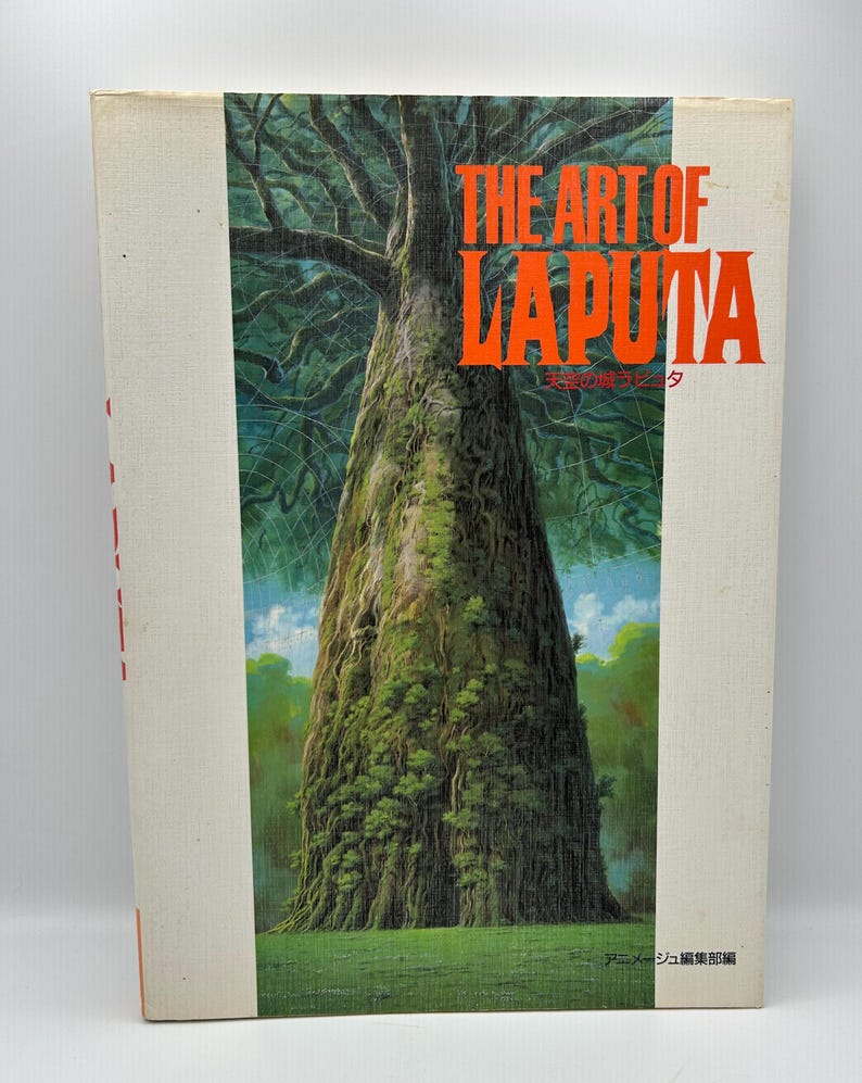 May include: A hardcover book titled "THE ART OF LAPUTA" with a vibrant illustration of a large tree. The cover art features a detailed painting of the tree's trunk and canopy, with green foliage and a blue sky.