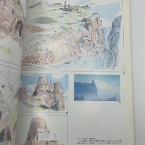 May include: Watercolor illustrations of a fantasy landscape with buildings and cliffs. The image is from a book, with Japanese text and numbers visible. The artwork depicts a village and a bridge.