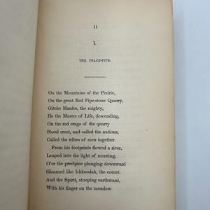 May include: Open book page with text from "The Peace-Pipe" poem. The page is aged with a cream color. The text is in black font. The top of the page has the number "11" and the Roman numeral "I."