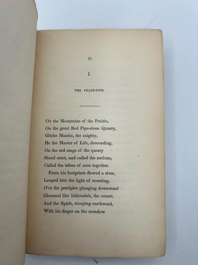 May include: Open book page with text from "The Peace-Pipe" poem. The page is aged with a cream color. The text is in black font. The top of the page has the number "11" and the Roman numeral "I."