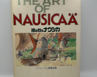 May include: A book titled "THE ART OF NAUSICAÄ" with Japanese text and an illustration of windmills. The cover is beige with red and green text. The illustration depicts a rural landscape with windmills.
