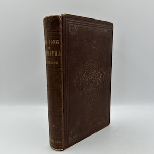May include: A vintage brown book titled "The Song of Hiawatha" by Longfellow. The cover features embossed floral designs and the spine displays the title and author's name. The book is in good condition, with some wear on the edges.
