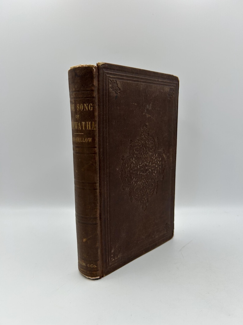 May include: A vintage brown book titled "The Song of Hiawatha" by Longfellow. The cover features embossed floral designs and the spine displays the title and author's name. The book is in good condition, with some wear on the edges.