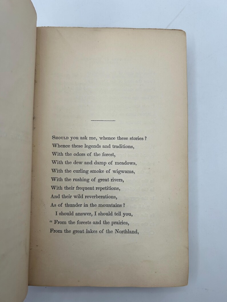 May include: Open book pages with printed text. The text begins with the question, "SHOULD you ask me, whence these stories?" and continues with a poem about legends, traditions, forests, rivers, and the Northland.