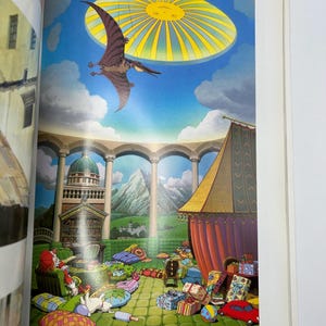 May include: A vibrant illustration from a book, featuring a pterodactyl soaring beneath a sun-like structure in a blue sky. The scene includes a building with columns, a tent, and colorful gifts, creating a whimsical atmosphere.