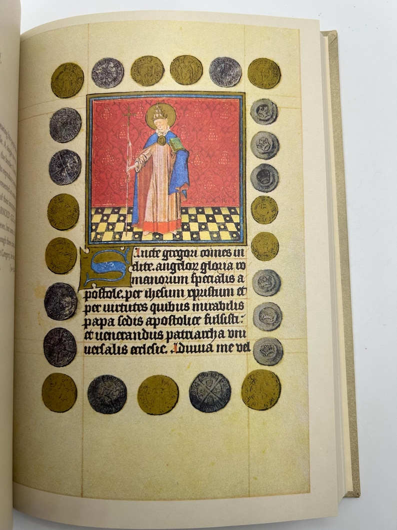 May include: Open book page featuring a medieval illustration. A central image depicts a robed figure with a halo, holding a staff, against a red backdrop. The page is bordered by gold and silver coin illustrations and includes handwritten text.