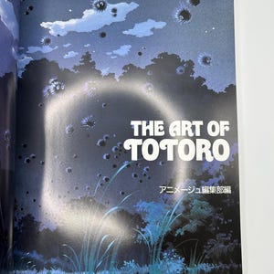 Puede incluir: Portada del libro "THE ART OF TOTORO" con letras blancas. La ilustraci&oacute;n muestra una escena nocturna de bosque en tonos azul oscuro y verde, con duendes de holl&iacute;n flotantes y texto japon&eacute;s.