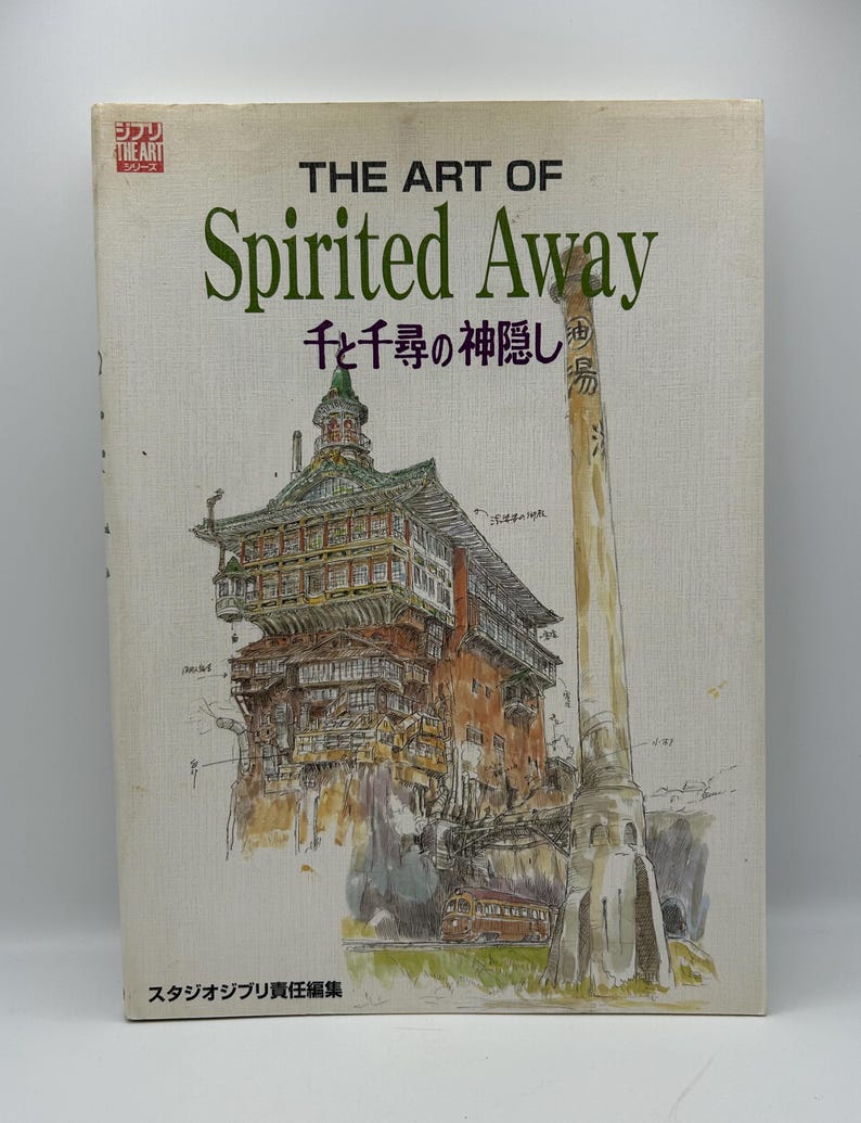 May include: A book titled "THE ART OF Spirited Away" with Japanese text and an illustration of a building and a tall structure. The cover is off-white with green and brown text and illustrations.