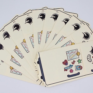 Puede incluir: Un abanico de tarjetas de color crema con un diseño de nevera de dibujos animados. Cada tarjeta presenta una cara sonriente y una nevera con imanes coloridos. Las tarjetas están dispuestas en semicírculo, mostrando el diseño lúdico.