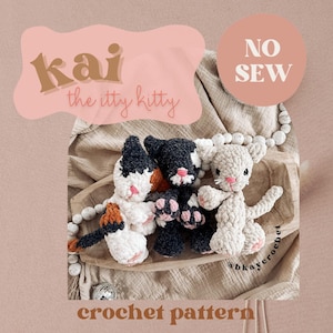 Könnte beinhalten: Drei gehäkelte Katzenspielzeuge in verschiedenen Farben: Weiß, Schwarz und Braun. Die Spielzeuge liegen auf einem Holztablett mit einer Perlenkette. Der Text "kai the itty kitty crochet pattern" und "NO SEW" ist im Bild zu sehen.