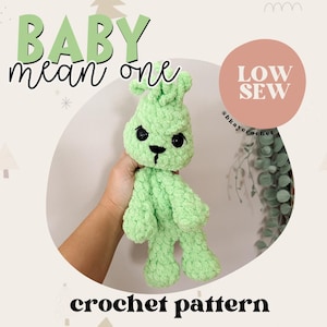 May include: A crochet pattern for a green baby bunny with black eyes and a black nose. The pattern is called "Baby Mean One" and is described as "Low Sew".