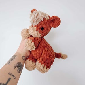 Puede incluir: Un peluche de caballo de ganchillo hecho a mano en tonos &oacute;xido y beige. El animal de peluche tiene un aspecto texturizado y suave con una melena y pezu&ntilde;as de color marr&oacute;n claro. El juguete se sostiene sobre un fondo blanco.