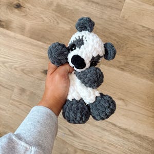 Peut inclure: Un jouet fait &agrave; la main en crochet repr&eacute;sentant un panda. Le panda a un corps blanc avec des accents gris sur les oreilles, les pattes et autour des yeux. Le nez de l'ours est noir et il a de petits yeux noirs. Le jouet est doux et moelleux.