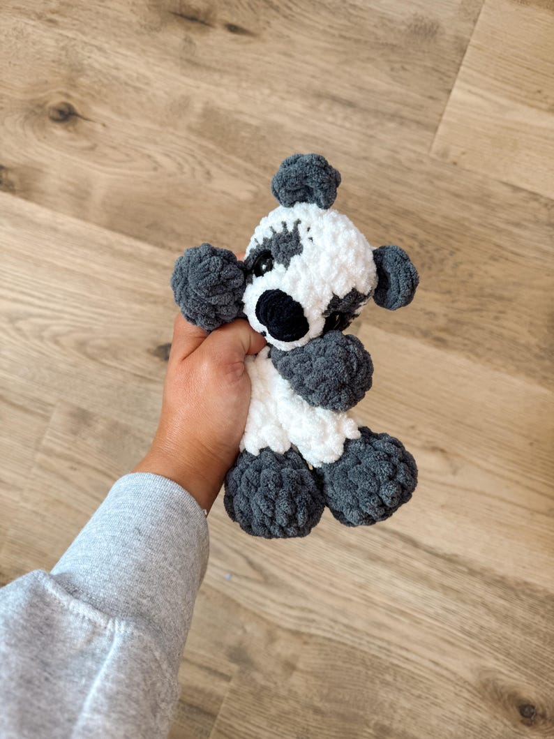 Peut inclure: Un jouet fait &agrave; la main en crochet repr&eacute;sentant un panda. Le panda a un corps blanc avec des accents gris sur les oreilles, les pattes et autour des yeux. Le nez de l'ours est noir et il a de petits yeux noirs. Le jouet est doux et moelleux.