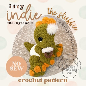 May include: A handmade crochet dinosaur toy in shades of green, orange, and white. The dinosaur has large black eyes and a fluffy white pom-pom on its head. The text "itty indie" and "crochet pattern" are visible.