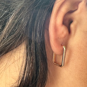 Può includere: Orecchini a cerchio quadrati in oro. Gli orecchini sono semplici e moderni, con un design elegante e minimalista.