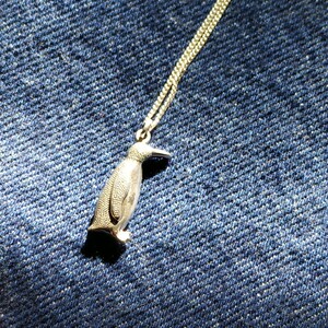 May include: A silver penguin pendant necklace. The penguin is detailed with textured feathers and a long beak. The chain is silver and has a delicate link.