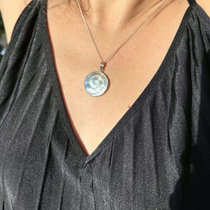 Puede incluir: Un collar de plata con un colgante redondo con un diseño de espiral de nácar blanco.