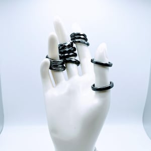 May include: A set of black hematite rings, stacked on a mannequin hand. The rings are all different sizes and styles, with some having a faceted design.