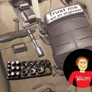 May include: A green canvas bag with a black zippered pouch that says "Trust me I am an engineer". The bag also contains a wrench, a socket wrench set, and a black and red cartoon sticker of a person with the name "Willem" on it.