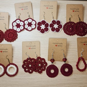 May include: Assortment of handmade crocheted earrings in burgundy and white. The earrings are displayed on brown cards with the text "Handmade with love".