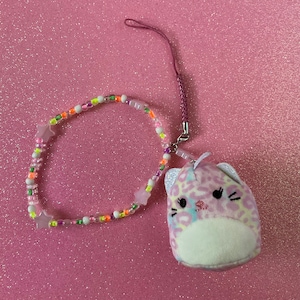 May include: A pink and white plush cat charm with a leopard print design. The charm is attached to a pink beaded necklace with white stars and colorful beads.