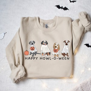 May include: A beige sweatshirt with a graphic of four dogs dressed as ghosts for Halloween. The dogs are holding pumpkins and the text "HAPPY HOWL-O-WEEN" is printed below them.