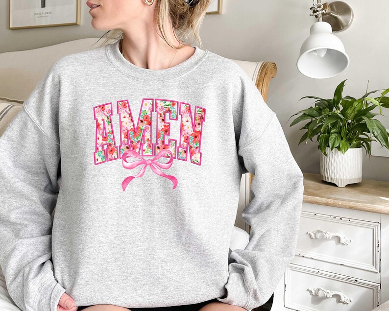 May include: A gray sweatshirt with a floral print of the word "AMEN" in pink and white. A pink bow is centered below the word.