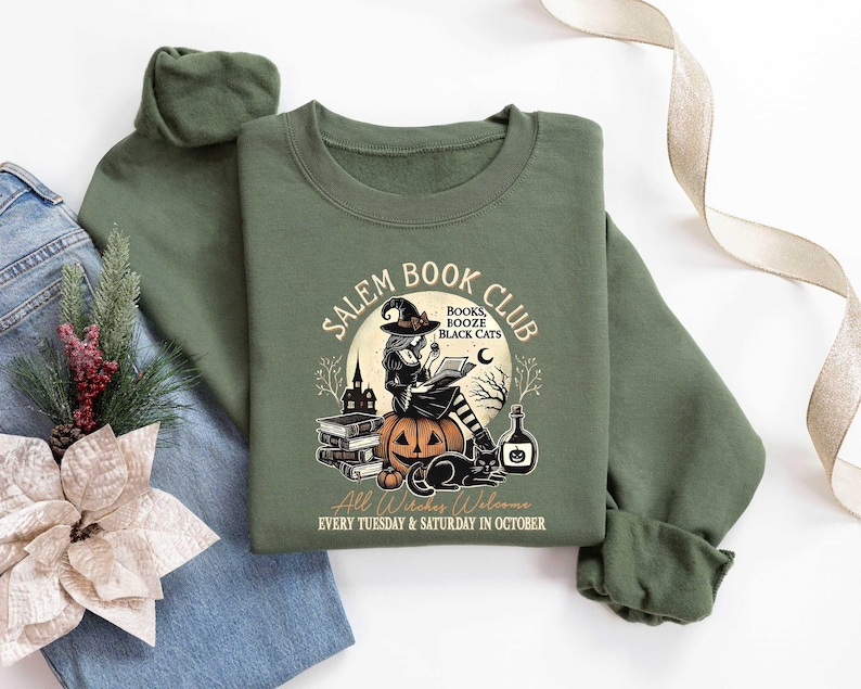 May include: Green sweatshirt with a graphic of a witch reading a book in front of a pumpkin and a black cat. The text reads "Salem Book Club" with the words "Books, Booze, Black Cats" and "All Witches Welcome" below the graphic. The text also says "Every Tuesday & Saturday in October".