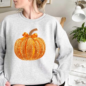 May include: A gray sweatshirt with a sparkly orange pumpkin design. The pumpkin has a brown stem and an orange ribbon.