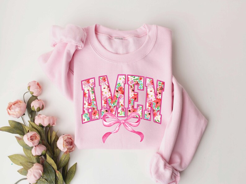 May include: Pink sweatshirt with a floral print "AMEN" design and a pink bow.